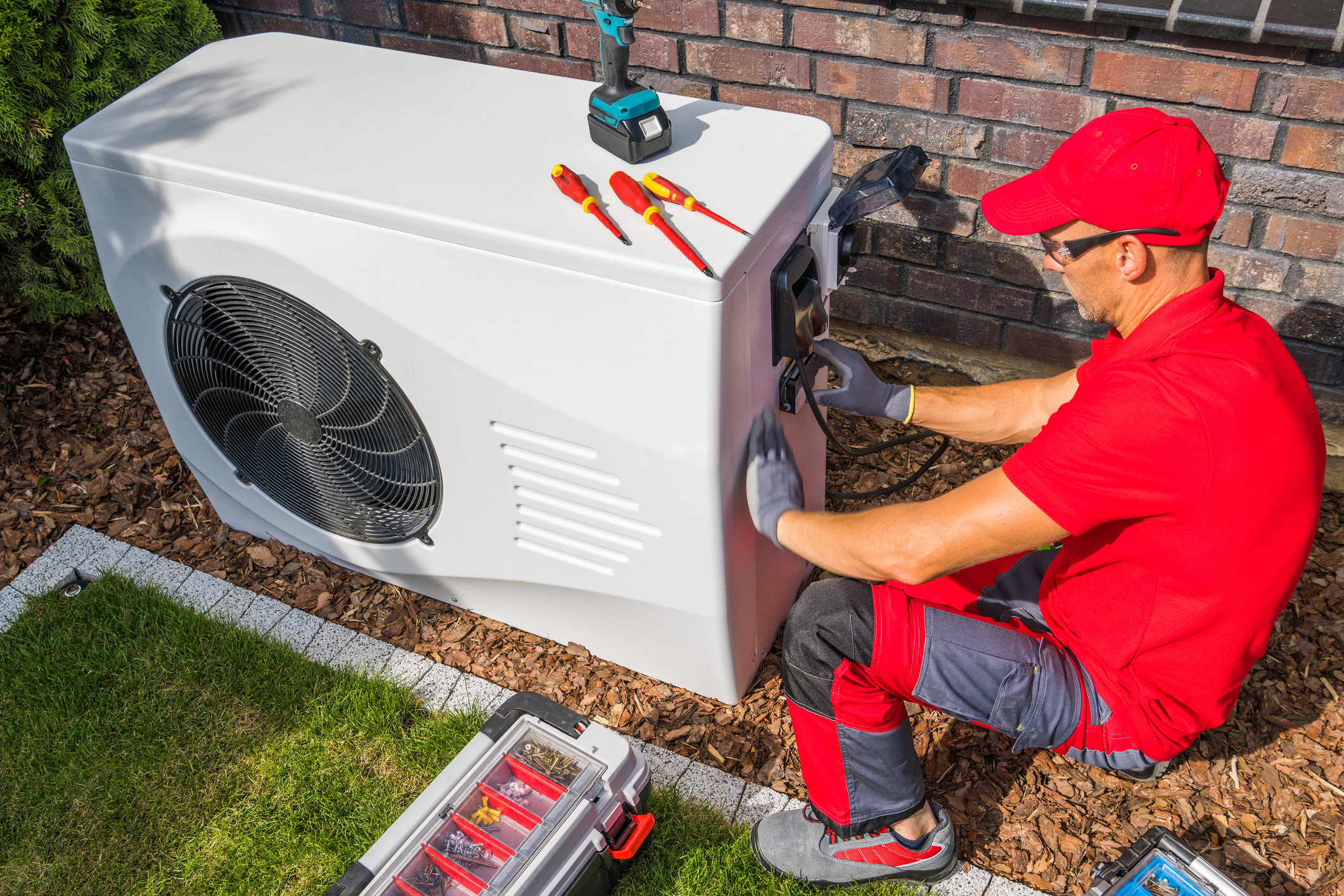 Professional Middle Aged HVAC Technician in Red Uniform Repairing Modern Heat Pump Unit